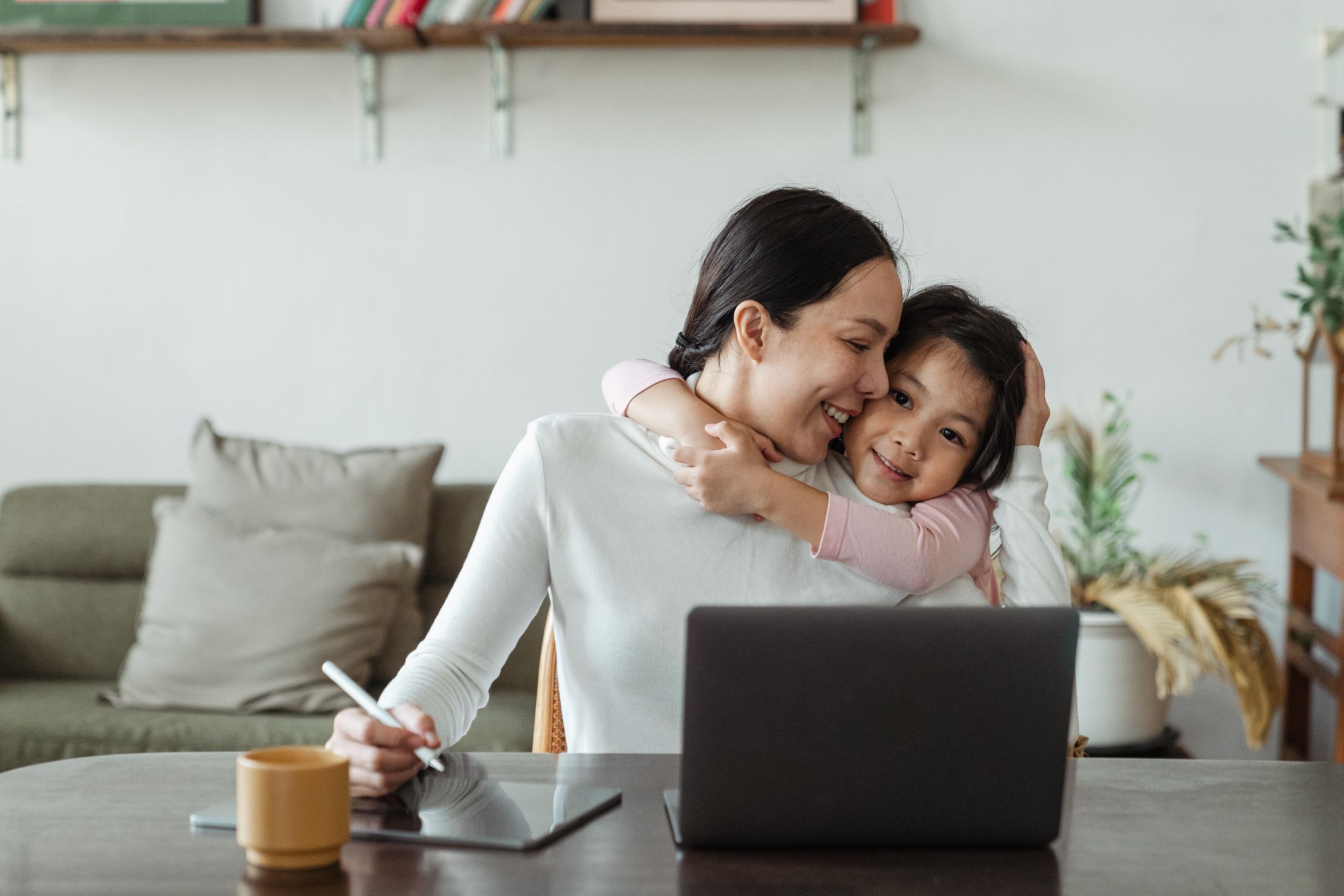 Illustrative stock: a mother working while her daughter hugs her